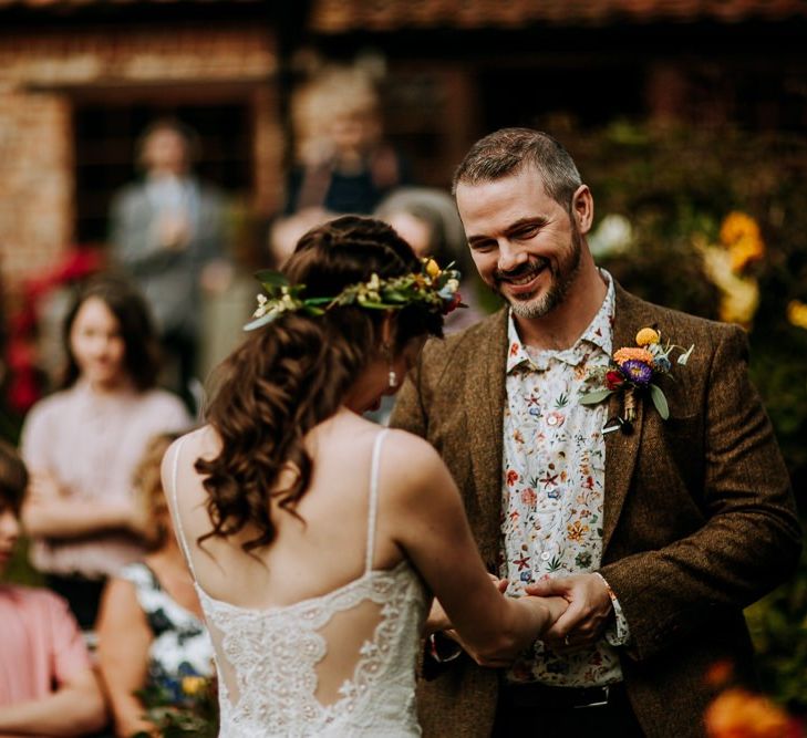 Groom in Wool Blazer and Floral Shirt Holding his Brides Hands During the Wedding Ceremony