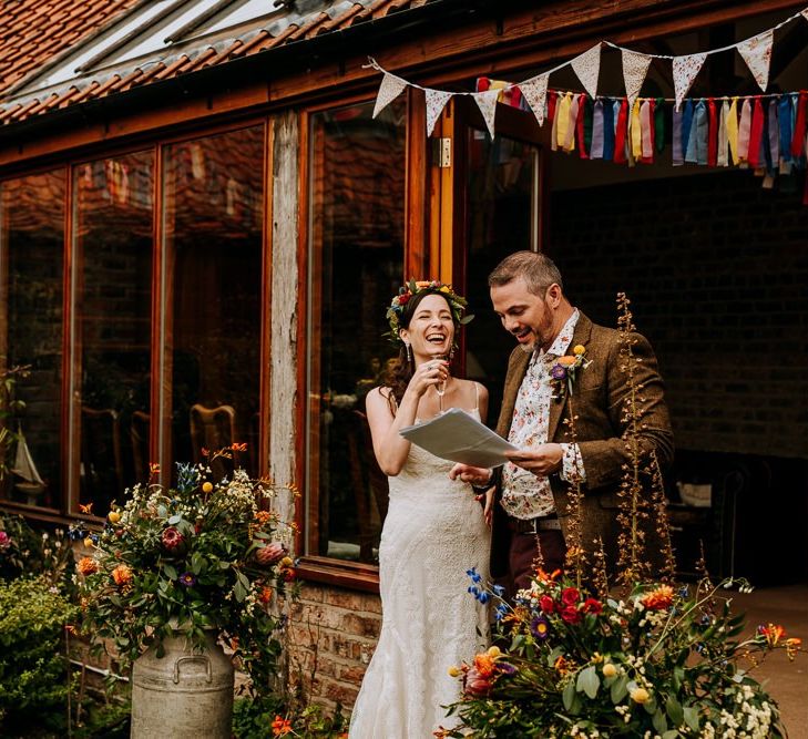 Bride in Sottero &amp; Midgley Wedding Dress and Colourful Flower Crown and Groom in Brown Wool Suit and Floral Shirt Laughing