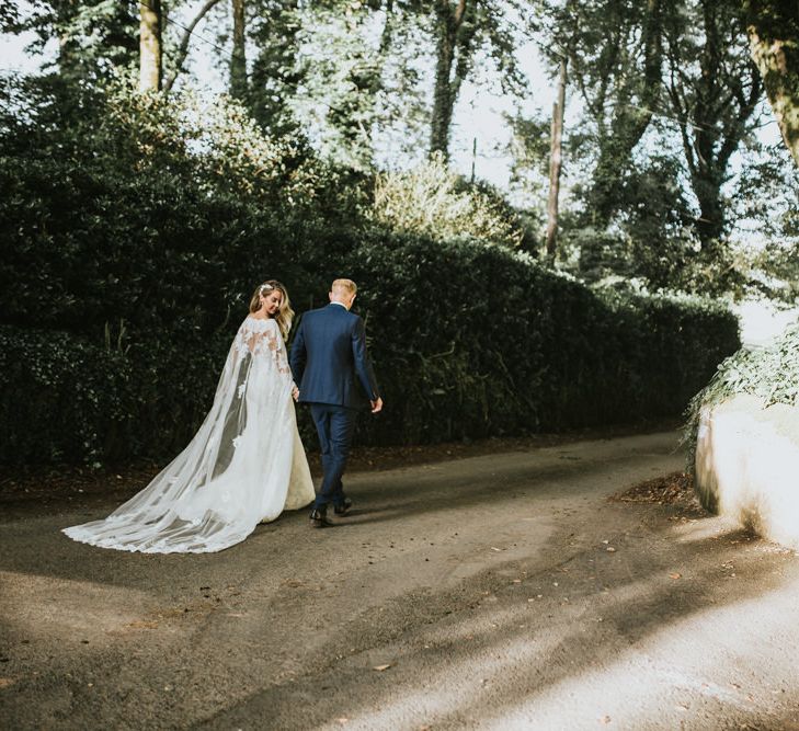 Bride in Pronovias Oringo Lace Bridal Gown &amp; Cape | Groom in Blue Marks and Spencer Suit | Green, White &amp; Gold Wedding at Buckland Tout Saints, Devon |  Darina Stoda Photography