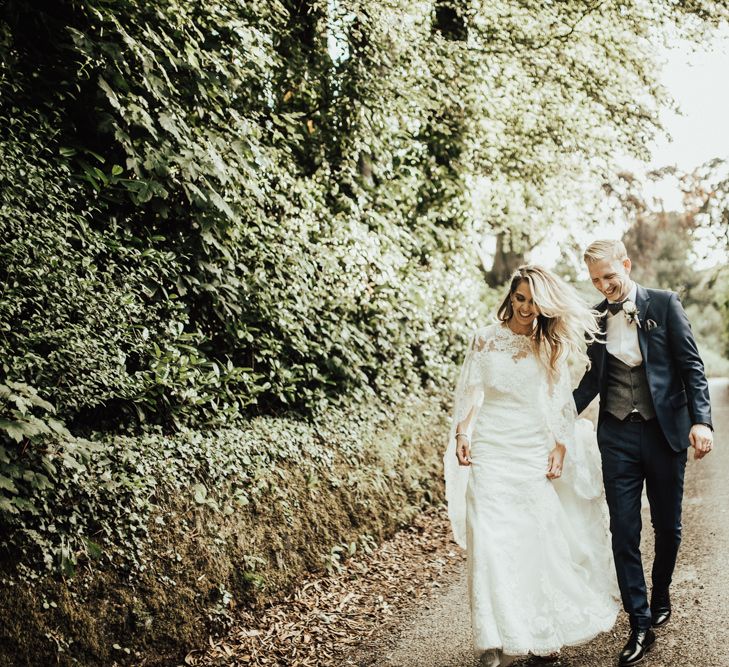 Bride in Pronovias Oringo Lace Bridal Gown &amp; Cape | Groom in Blue Marks and Spencer Suit | Green, White &amp; Gold Wedding at Buckland Tout Saints, Devon |  Darina Stoda Photography