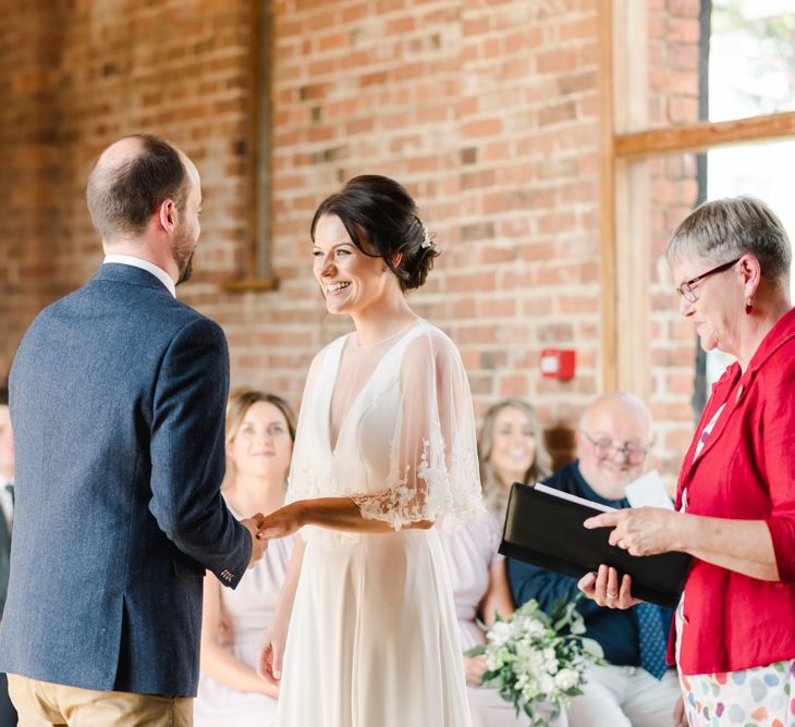 Bride in lace overlay jacket with groom during ceremony