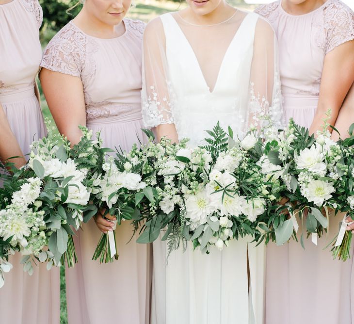 Bridesmaids in blush dresses holding white wedding flowers