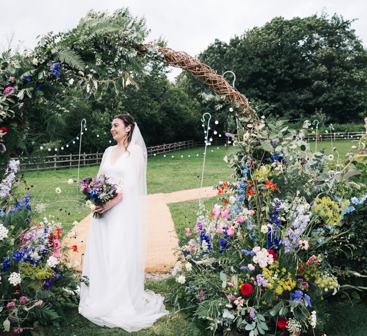 Bride in lace sleeved wedding dress with flower moon gate arch