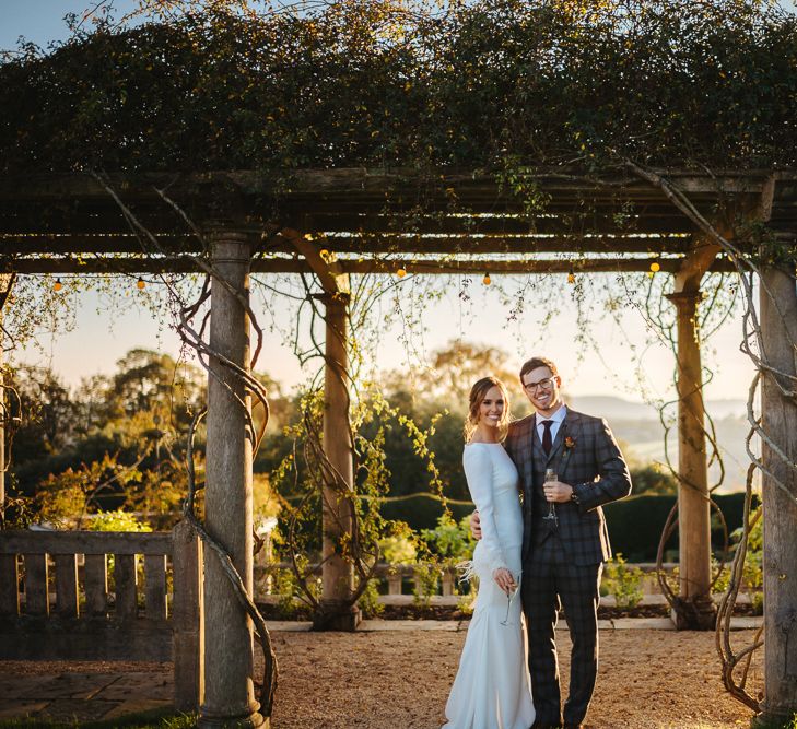 Bride in Fitted Pronovias Wedding Dress with Long Sleeves and Groom in Grey Checked Suit