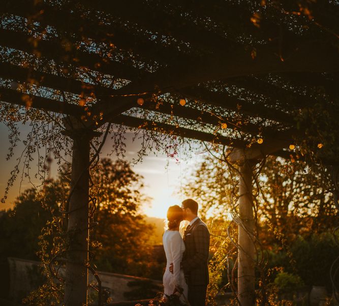 Sunset Wedding Portrait of Bride in Long Sleeve  Pronovias Wedding Dress and Groom in Grey Checked Suit