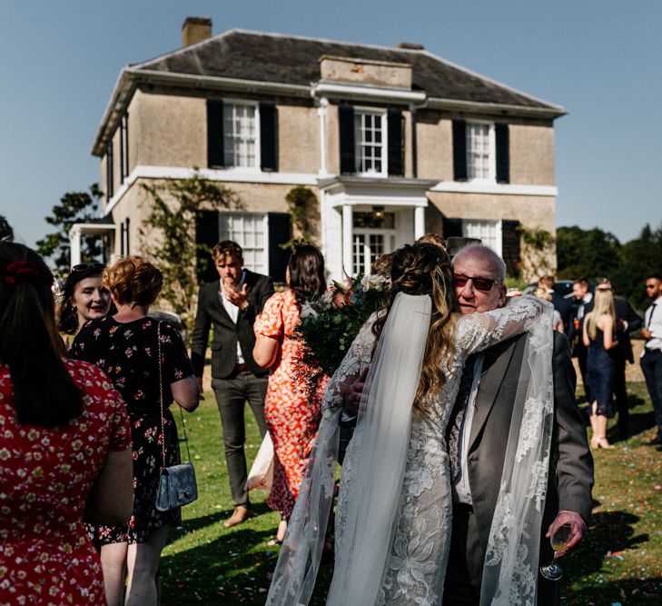 Bride in bell sleeve bridal gown hugging wedding guest