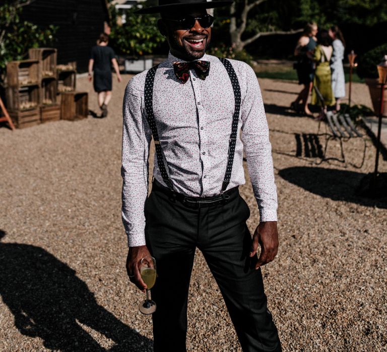 Stylish wedding guest in floral shirt, braces, bow tie and top hat