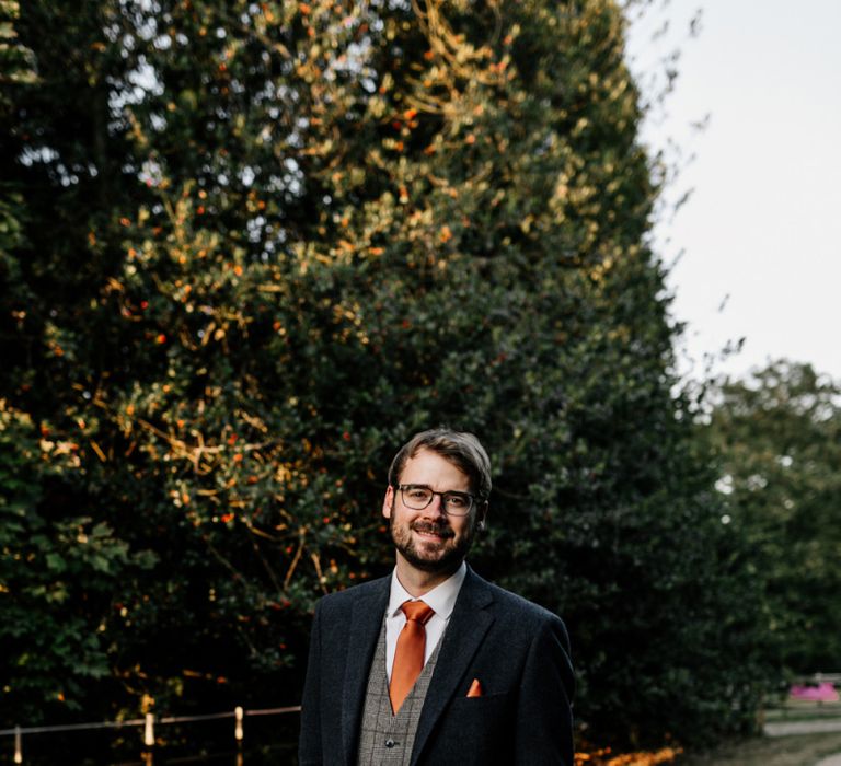 Groom in navy wool suit with check waistcoat and orange tie