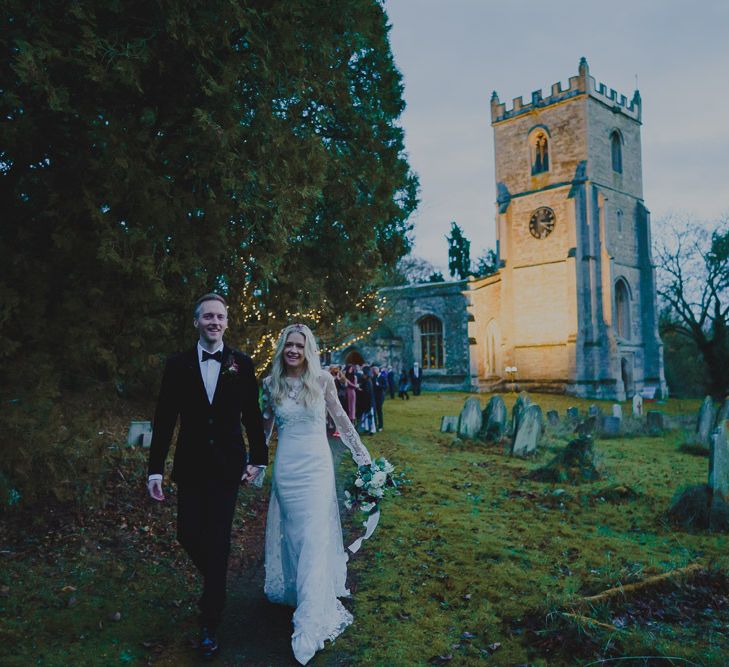 Bride and groom, followed by their guests, walking through the country lane