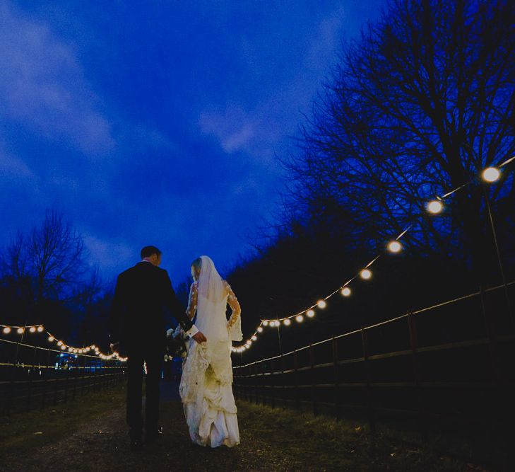 Bride and groom walking down a country lane covered in festoon lights