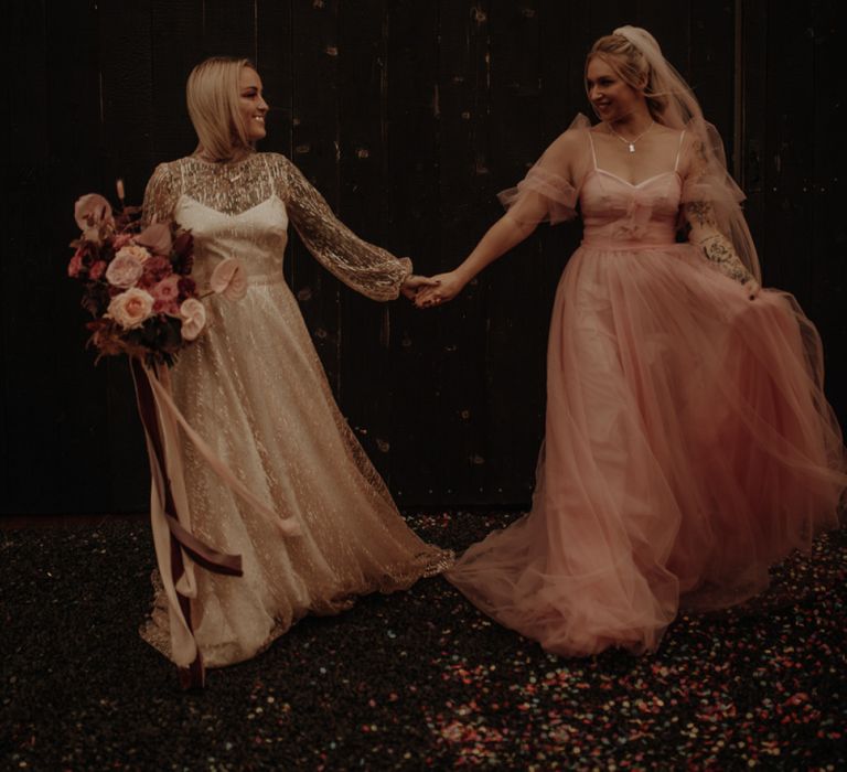 Two brides holding hands in gold glitter and pink dress for wedding inspiration at The Giraffe Shed