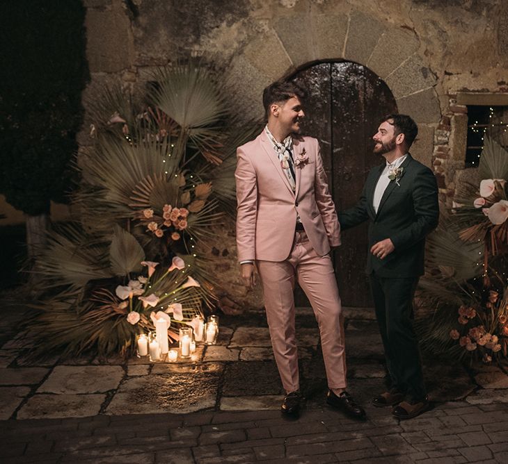 Same Sex Grooms  in Pink and Green Wedding Suits Standing Neck to Candles