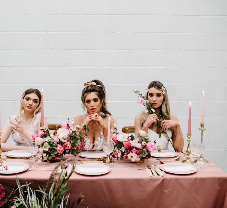 Brides Sitting at Pink Tablescape with Pink Table Cloth and Deep Pink Floral Arrangement