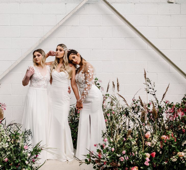 Three Brides Standing by Deep Pink and Foliage Floral Arrangements