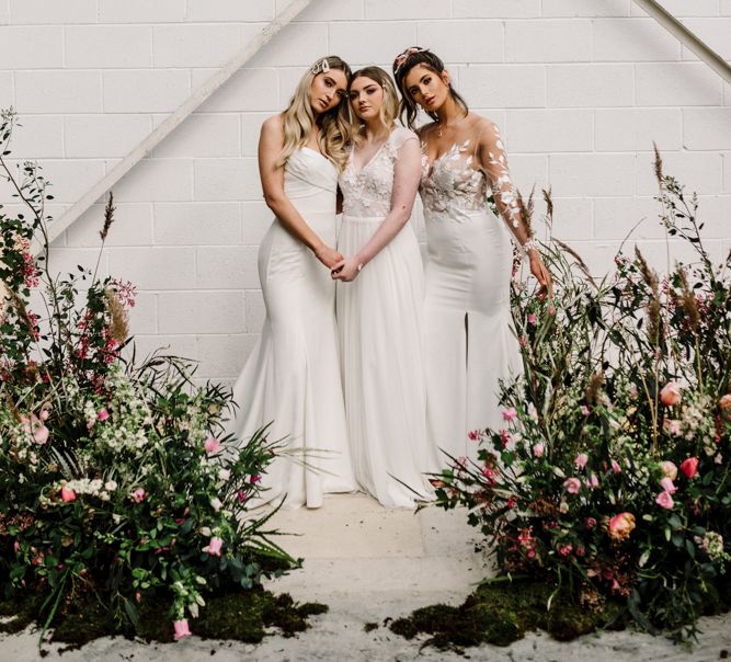 Three Brides Standing by Deep Pink and Foliage Floral Arrangements