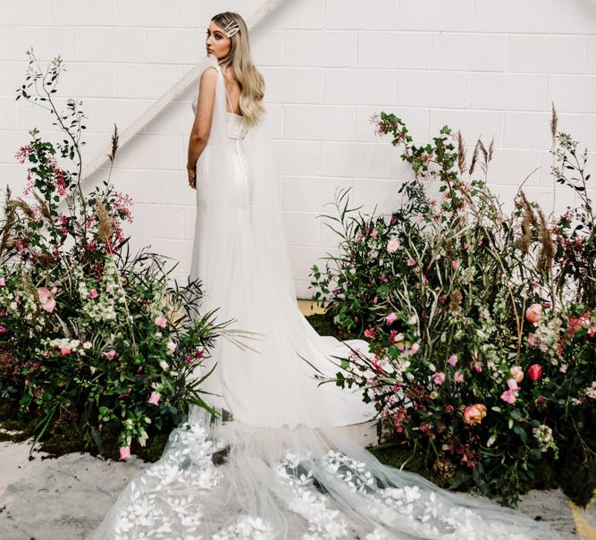 Bride with  Long Lace Wedding  Train Standing by Deep Pink and Foliage Floral Arrangements