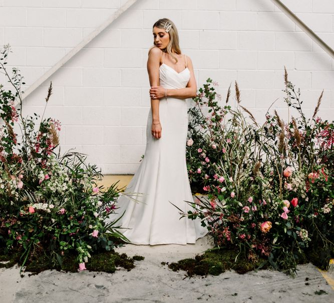 Bride in Fitted Wedding Dress Standing by Deep Pink and Foliage Floral Arrangements