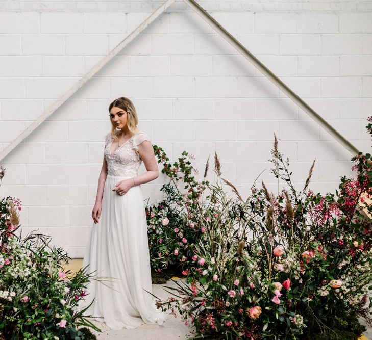 Bride in Lace Bodice and Floaty Skirt Wedding Dress  Standing by Deep Pink and Foliage Floral Arrangements