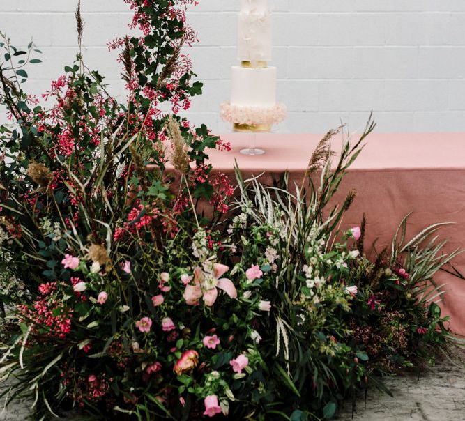 Elegant Wedding Cake with Round and Square Layers Next to Deep Pink and Foliage Floral Arrangement