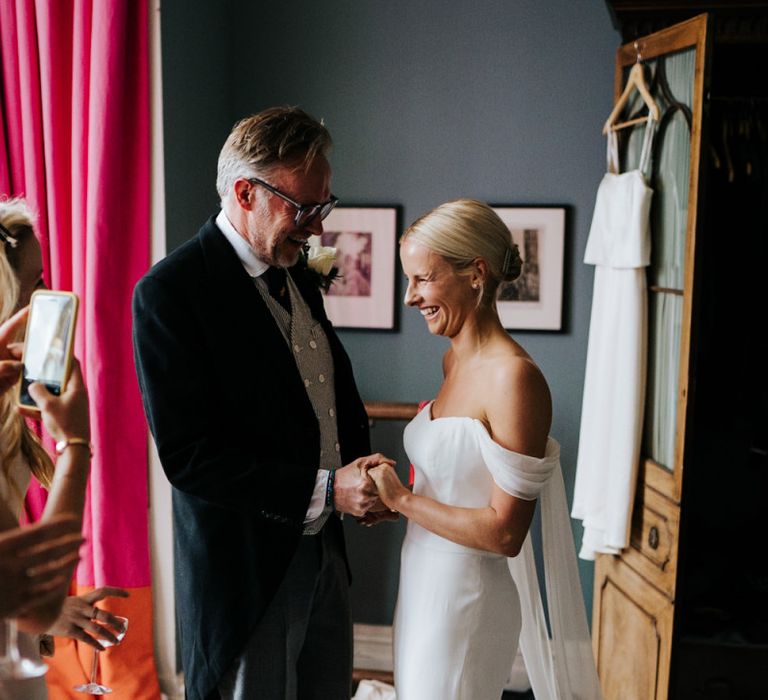 Father of the bride and bride hold hands as he sees her in her dress for the first time