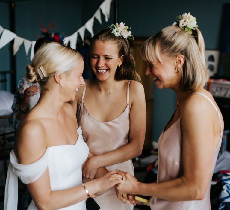 Bride holds hands and smiles at two sister in excited anticipation for the wedding ceremony