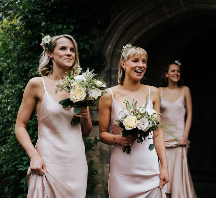 Bridesmaids hold bouquets and smile at bride, off-frame, as she enters her wedding car