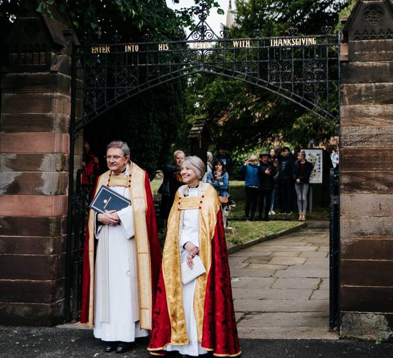 Vicars patiently await arrival of the bride outside of the village church in Hawarden, Wales