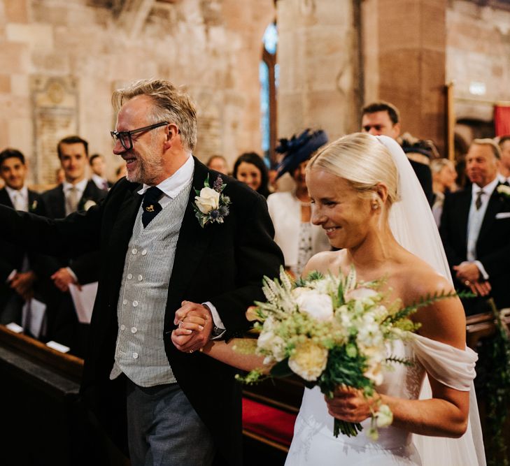 Bride and father of the bride arrive at the front of the aisle and hug the groom