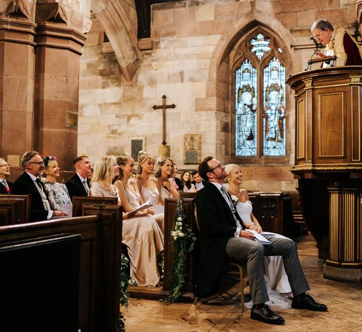 Bride and groom, and bride's family listen attentively to vicar's sermon and smile while doing so