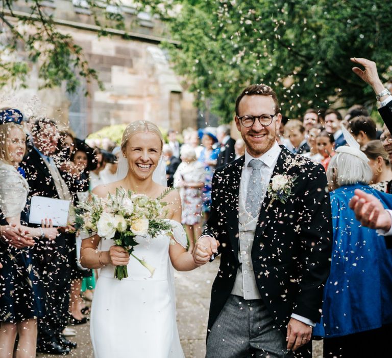 Bride and groom exit the church and walk down the pathway as guests throw confetti at them