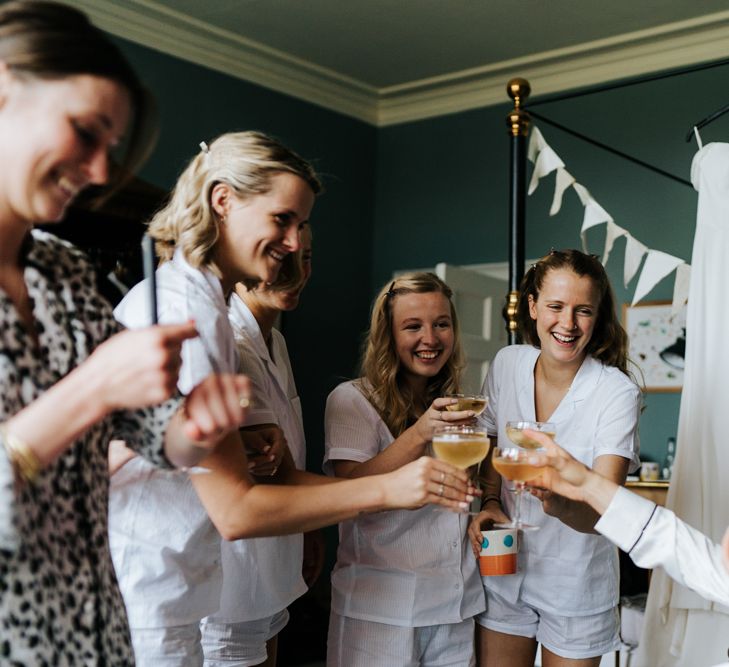 Bride and bridesmaids each hold a glass of champagne and say a toast for the day ahead