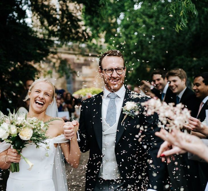 Bride and groom exit the church and walk down the pathway as guests throw confetti at them