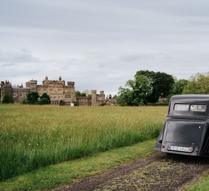 Bride and groom drive towards Hawarden Castle in beautiful, black vintage car