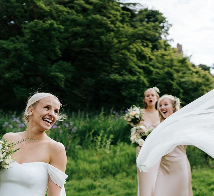 Bride's veil flies out of her hair as bridesmaids look on in amazement