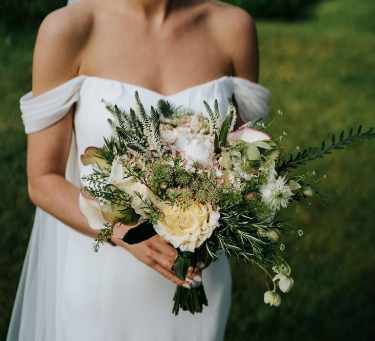 Bride in off the shoulder wedding dress holding a cream rose and foliage wedding bouquet