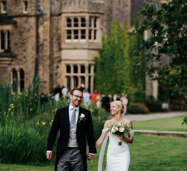 Bride and groom walk towards camera with Hawarden Castle in the background