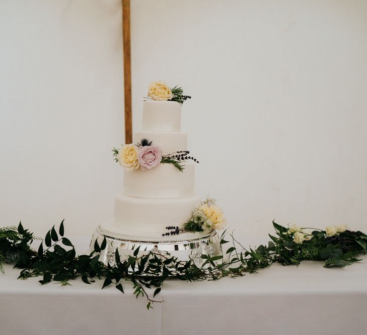 Three-tiered, white wedding cake with yellow and pink roses as decoration