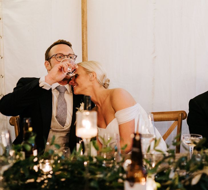 Bride embraces groom, as he takes a drink of wine, after he has completed his speech