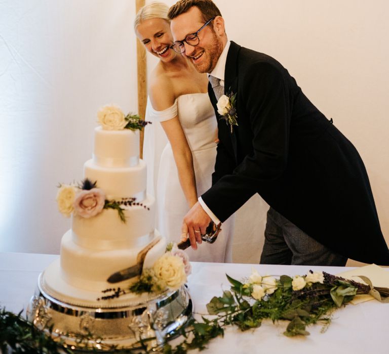 Bride and groom smile as they cut the wedding cake with a sword