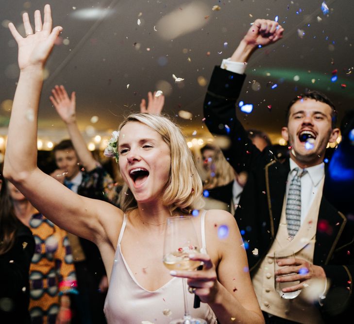 Sister of the bride and guests smiling and cheering as confetti explodes over the dancefloor