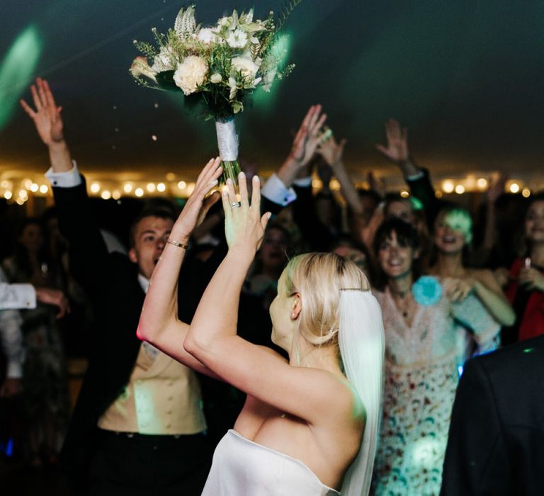 Bride throws bouquet into crowd of keen guests on the dancefloor