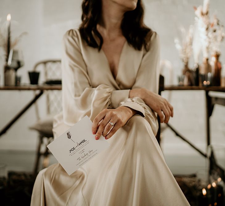 Bride in Oyster Coloured Satin Wedding Dress Holding a Contemporary Wedding Invitation