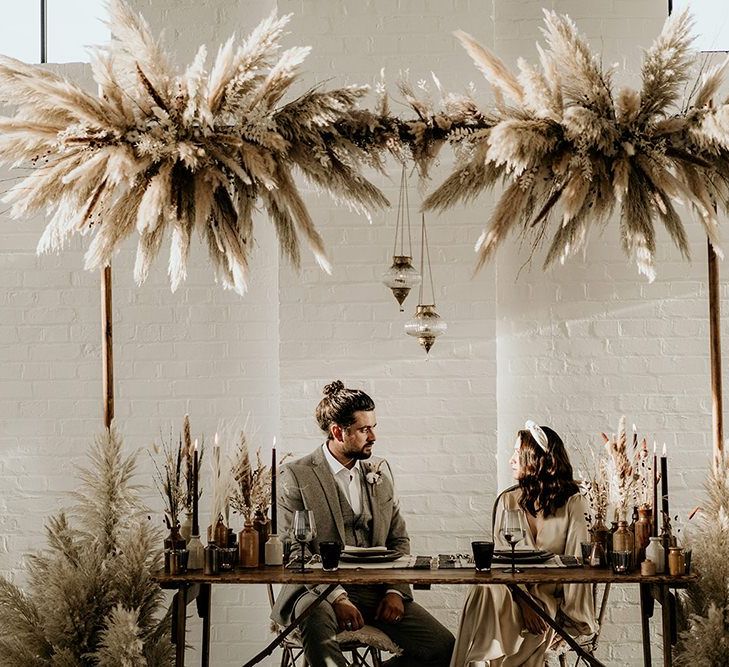 Bride and Groom Sitting at a Sweetheart Table with Pampas Grass Installation