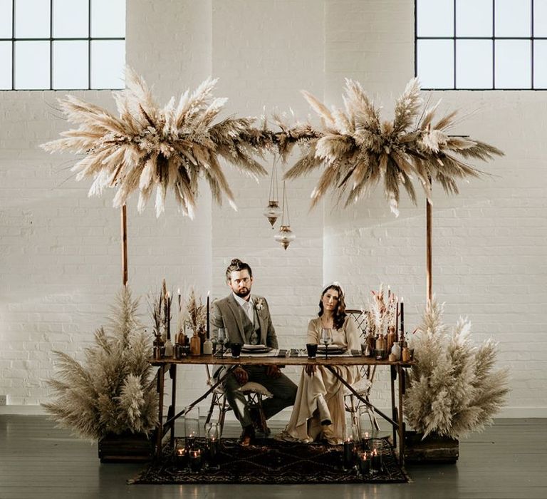 Stylish Bride an Groom Sitting at a Boho Tablescape with Pampas Grass Hanging Installation