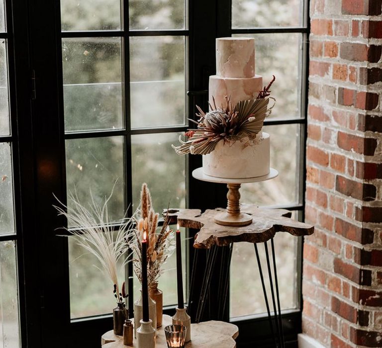 Wedding Cake Decorated with a King Protea Standing on a Wooden Table with Metal Legs