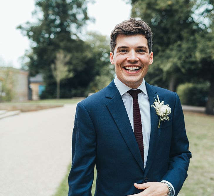 Groom in Navy Suit from Hackett and Burgundy Tie from Gucci with Floral Buttonhole