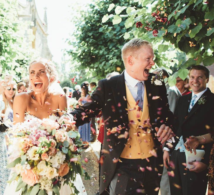 Confetti Moment with Bride in Halfpenny London Wedding Dress Holding a Blush, White and Green Bouquet and Groom in Traditional Morning Suit