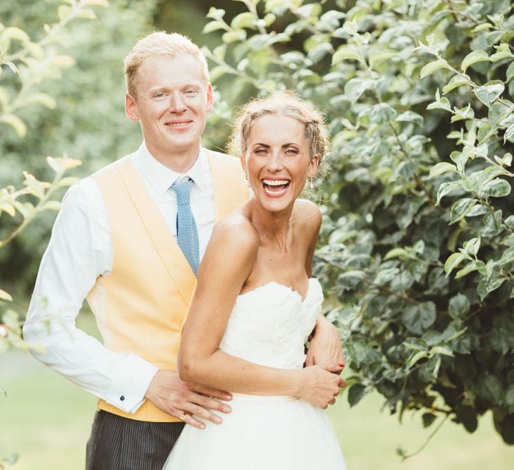 Bride in Tulle and Applique Halfpenny London Wedding Dress with Groom in Yellow Waistcoat and Blue Tie Embracing