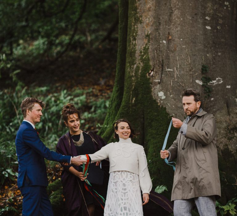 Bride in Crochet Wedding Dress and Woollen Jumper and Groom in Navy Suit Holding Hands During the Wedding Ceremony