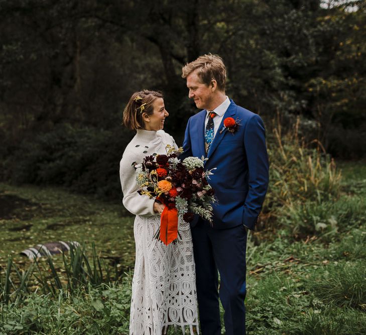 Bride in Crochet Wedding Dress and Woollen Jumper and Groom in Navy Paul Smith Suit Laughing by the Steam